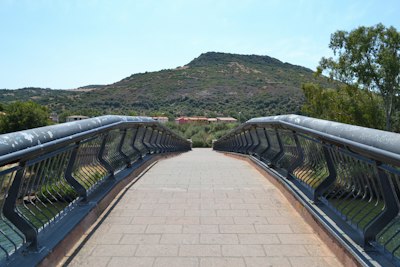 A modern pedestrian bridge leads to a green hill